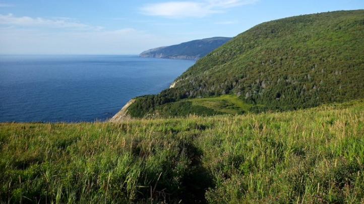 Green Cape Breton hills immersing with the dark blue ocean