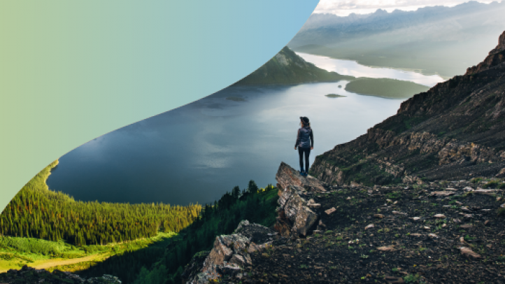 Person standing on a cliff overlook a water and mountains 